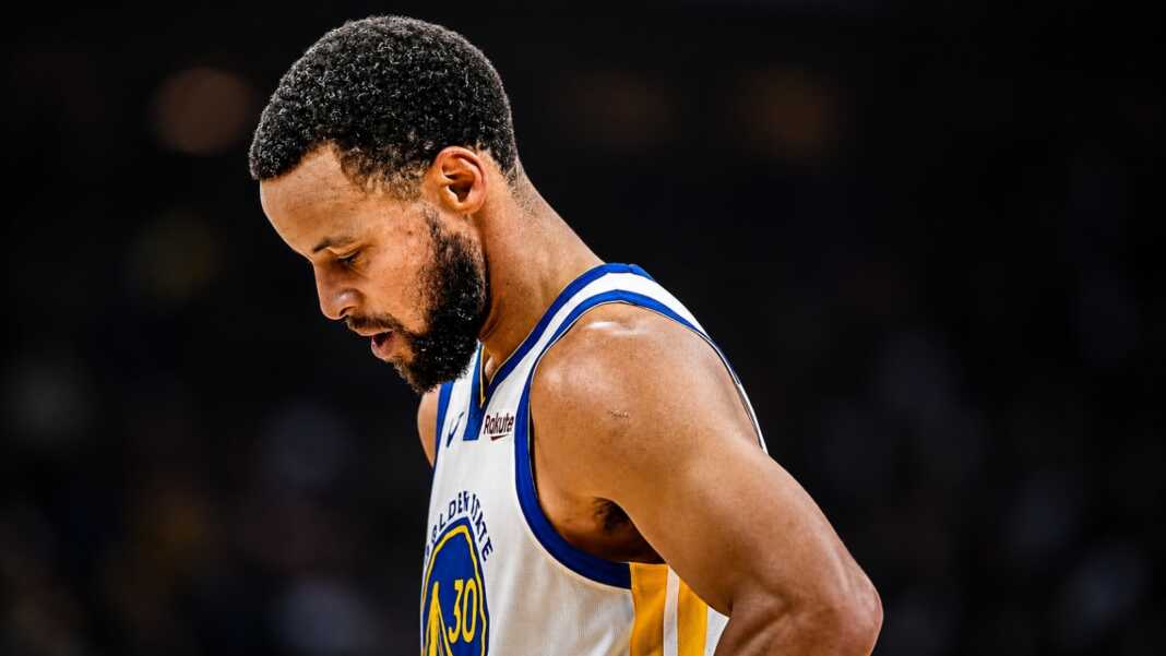 Stephen Curry menunduk di lapangan saat mengenakan jersey Golden State Warriors.